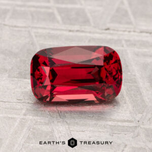 A 1.76-carat rectangular cushion-cut red spinel rests on a light gray textured surface, with the text "EARTH'S TREASURY" displayed below.