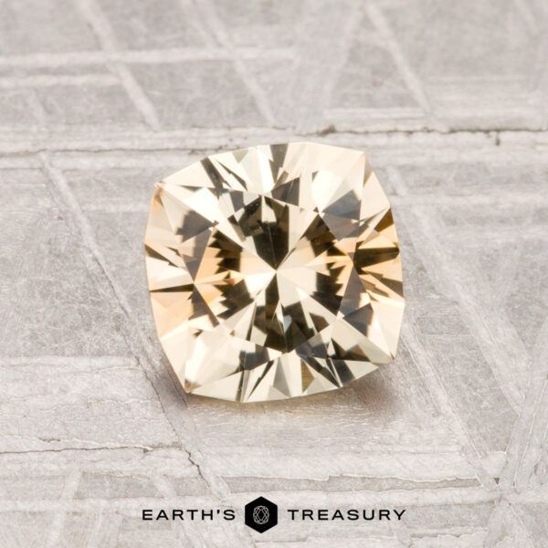 1.37-Carat Montana Sapphire (Heated) A faceted, light yellow 1.37-carat heated Montana sapphire is displayed on a patterned gray surface with "EARTH'S TREASURY" text at the bottom.