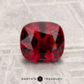 A 1.54-carat cushion-cut red Spinel is displayed on a textured light gray surface with "EARTH'S TREASURY" at the bottom.