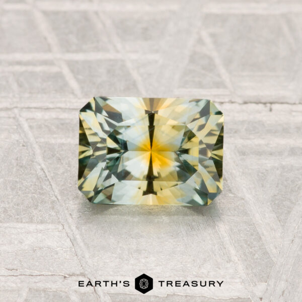 1.16-Carat Montana Sapphire (Heated) A rectangular, multi-colored 1.16-carat Montana Sapphire (Heated) with yellow and green hues is displayed on a textured surface with "EARTH'S TREASURY" below.