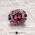 A 1.78-carat heated Montana sapphire with a round, faceted cut and pink-purple hue is displayed on a textured light gray surface, featuring the text "EARTH'S TREASURY" at the bottom.