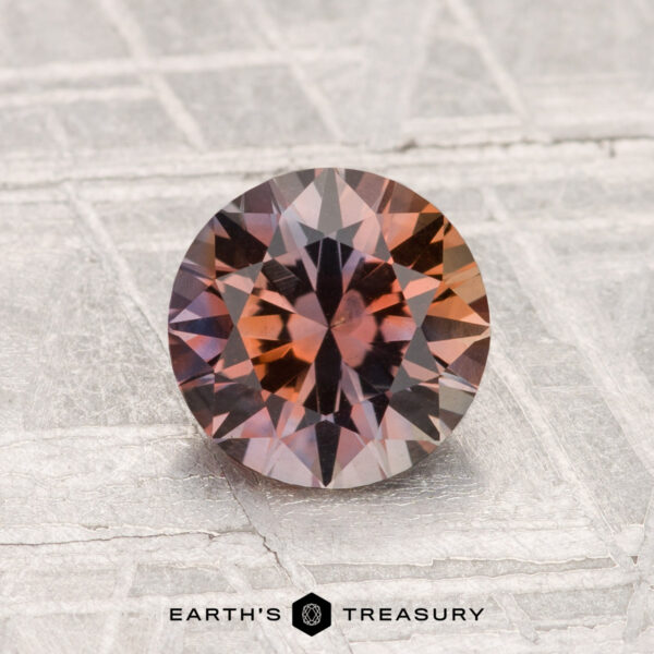 1.45-Carat Montana Sapphire (Heated) A 1.45-carat heated Montana sapphire with reddish-brown and purple tones is displayed on a textured metallic background featuring the text “EARTH’S TREASURY” at the bottom.