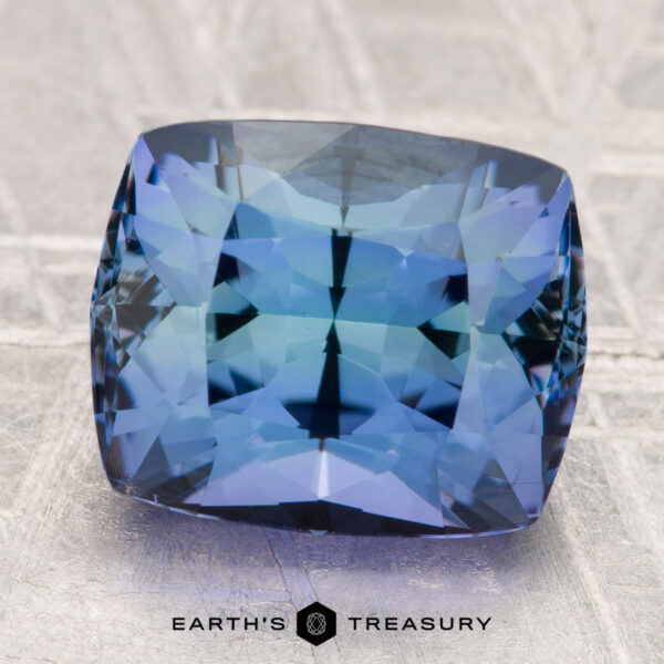 6.30-Carat Unheated Tanzanite (Zoisite) A 6.30-carat unheated tanzanite (zoisite) with stunning internal reflections rests on a textured grey surface, with "EARTH'S TREASURY" displayed below.