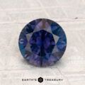 A 2.12-carat round-cut heated Montana sapphire is displayed on a textured pale surface with "EARTH'S TREASURY" at the bottom.