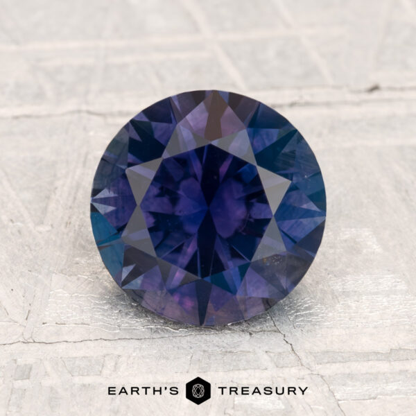2.12-Carat Montana Sapphire (Heated) A 2.12-carat round-cut heated Montana sapphire is displayed on a textured pale surface with "EARTH'S TREASURY" at the bottom.