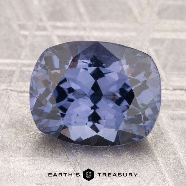 3.33-Carat Spinel A faceted, cushion-cut 3.33-carat blue Spinel rests on a light, textured surface with the "Earth's Treasury" logo below.