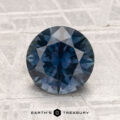 A 2.12-carat heated Montana sapphire, round and faceted with a blue hue, rests on a textured light surface. "EARTH'S TREASURY" is shown at the image's bottom.