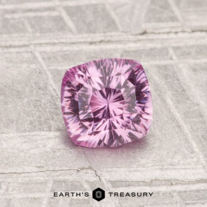 A 1.06-carat, cushion-cut pink sapphire rests on a metallic patterned surface, with "EARTH'S TREASURY" shown below.