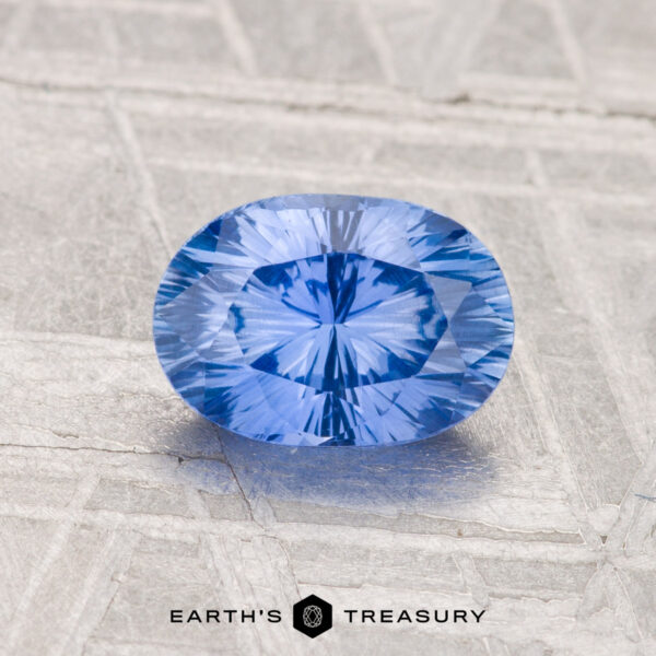 1.24-Carat Ceylon Sapphire (Heated) A 1.24-carat heated Ceylon sapphire, faceted in an oval shape, rests on a textured gray surface with the "Earth's Treasury" logo at the bottom.