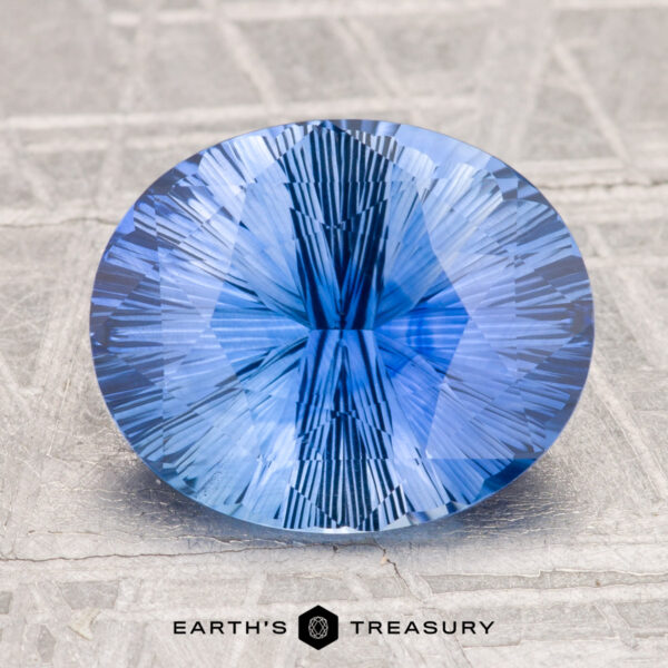 3.91-Carat Ceylon Sapphire (Heated) 3.91-Carat Ceylon Sapphire (Heated), oval-cut with intricate facets and a light violet-blue hue, displayed on a textured light gray surface, "EARTH'S TREASURY" text at the bottom.