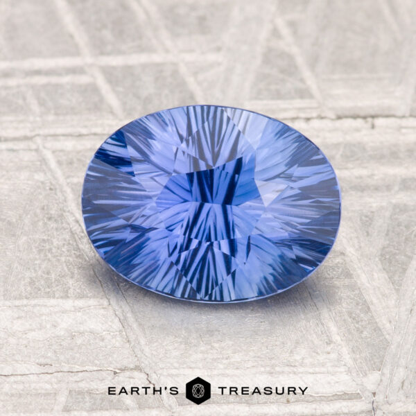 1.93-Carat Ceylon Sapphire A 1.93-carat Ceylon sapphire, faceted in an oval shape with intricate internal patterns, rests on a textured metallic surface. The “Earth’s Treasury” logo appears at the bottom.