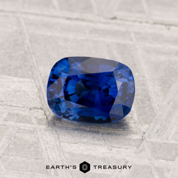1.18-Carat Ceylon Sapphire (Heated) A 1.18-carat heated Ceylon sapphire, cushion-cut and deep blue, is displayed on a textured gray surface with the text "EARTH'S TREASURY" below.