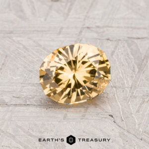 A round, faceted 0.87-carat Grossular Garnet gemstone is displayed on a textured gray surface with the text "EARTH'S TREASURY" at the bottom.