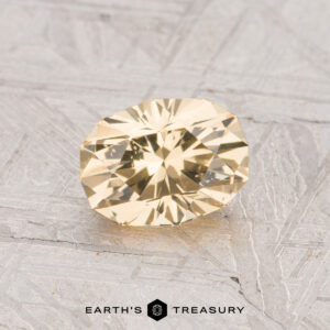 A 1.10-carat yellow grossular garnet gemstone is displayed on a textured gray surface with the text "EARTH'S TREASURY" at the bottom.