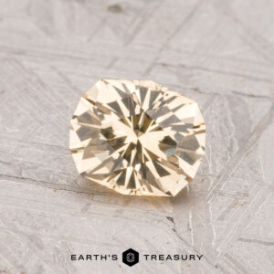 A 0.96-carat round, faceted pale yellow Grossular Garnet is displayed on a textured gray surface with the text “Earth’s Treasury” at the bottom.