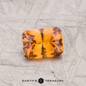 A 0.74-carat Grossular Garnet gemstone rests on a textured gray surface with "EARTH'S TREASURY" text and logo at the bottom.