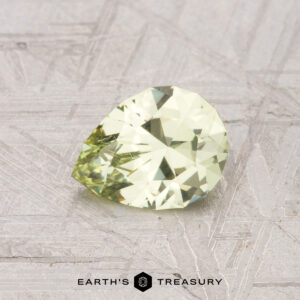 A 0.89-carat, pear-shaped grossular garnet with a light yellow hue rests on a textured metallic surface featuring the text "Earth's Treasury" below.