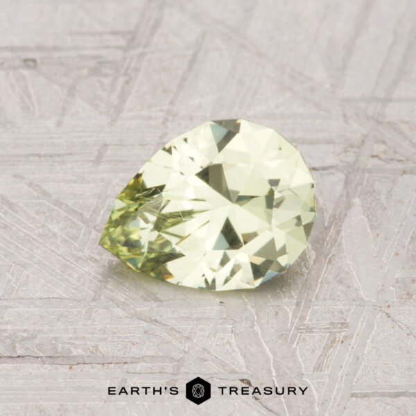 0.89-Carat Grossular Garnet A 0.89-carat, pear-shaped grossular garnet with a light yellow hue rests on a textured metallic surface featuring the text "Earth's Treasury" below.