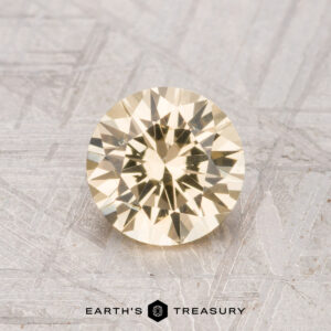 A 0.99-carat Grossular Garnet, round and pale yellow with facets, is shown on a textured gray surface above the "Earth's Treasury" logo and text.