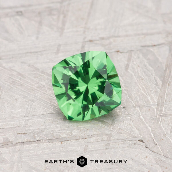 0.55-Carat Tsavorite Garnet A 0.55-carat cushion-cut Tsavorite garnet rests on a textured gray surface, with “EARTH'S TREASURY” displayed at the bottom.