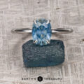 The "Tiara" ring in 18k white gold, featuring a 2.85-carat Montana sapphire, is displayed on a rough blue stone background with the Earth's Treasury logo at the bottom.