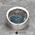 The Wide “Borealis” Ring in Blue-Violet Sapphire, featuring an intricate inner design, is shown upright on a rough blue stone with Earth's Treasury branding below.