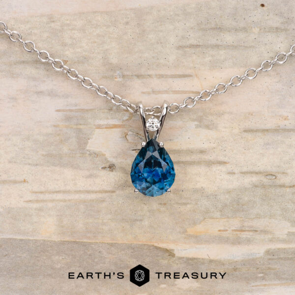 The "Brisa" pendant in 14K white gold with 1.25-carat Montana sapphire The "Brisa" pendant in 14K white gold showcases a pear-shaped 1.25-carat Montana sapphire with a small round white gemstone above it, displayed on a light textured background.
