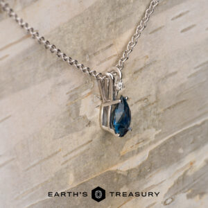 The "Brisa" pendant in 14K white gold features a 1.25-carat marquise-cut Montana sapphire on a silver chain, displayed on light wood. "EARTH'S TREASURY" logo appears at the bottom.