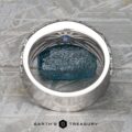 The Thin "Borealis" ring in 14k white gold features an intricate design and a small blue gemstone, displayed upright on a rough blue mineral with a geometric backdrop and the “Earth’s Treasury” logo below.