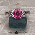 The "Saorise" ring in 14K white gold, featuring a 1.86-carat Mahenge garnet, is displayed on a rough dark green stone with the "Earth's Treasury" logo below on a textured surface.