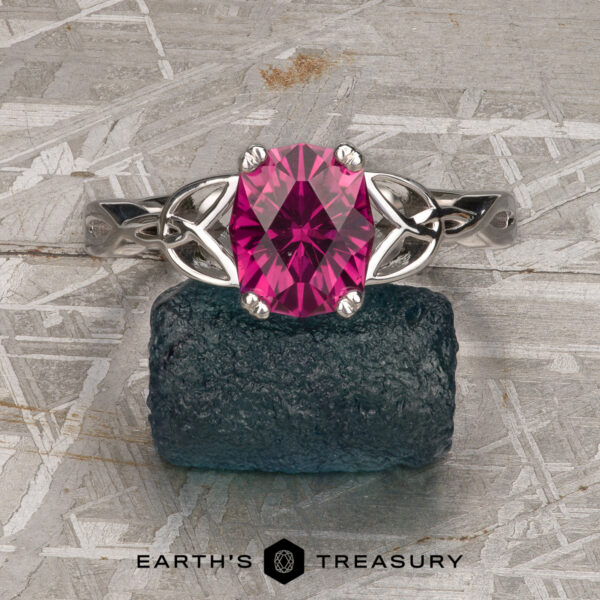 The "Saorise" ring in 14K white gold with 1.86-Carat Mahenge garnet The "Saorise" ring in 14K white gold, featuring a 1.86-carat Mahenge garnet, is displayed on a rough dark green stone with the "Earth's Treasury" logo below on a textured surface.