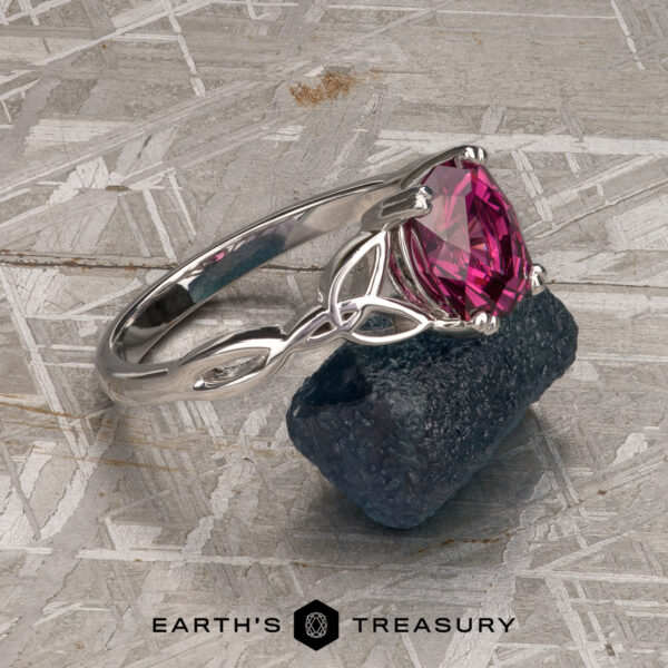 The "Saorise" ring in 14K white gold with 1.86-Carat Mahenge garnet The "Saorise" ring in 14K white gold featuring a 1.86-carat pink Mahenge garnet is displayed on rough blue stone atop a textured gray surface, with "EARTH'S TREASURY" at the bottom to showcase its elegant design.