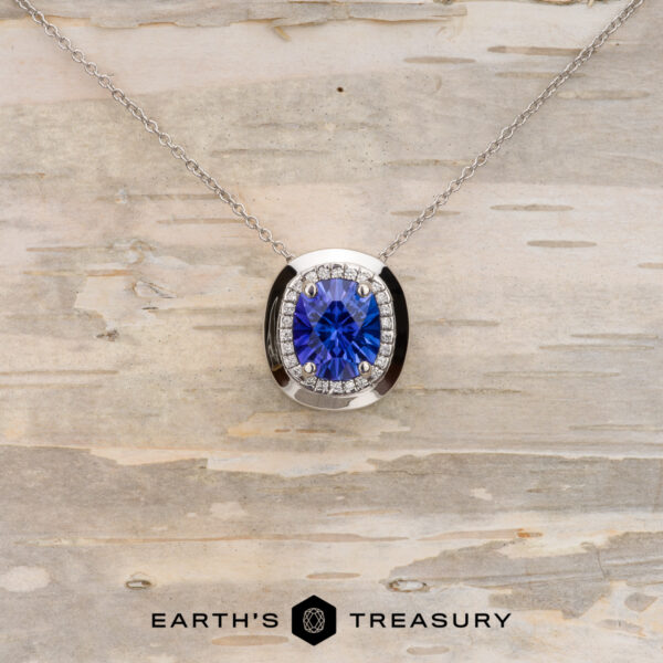 The Cirrus" Necklace in 14K white gold with 2.73-Carat Tanzanite A 14K white gold "The Cirrus" Necklace featuring a 2.73-carat cushion-cut tanzanite, accented by small clear stones, displayed on light wood with the "Earth's Treasury" logo at the bottom. Build your own unique pendant style today.