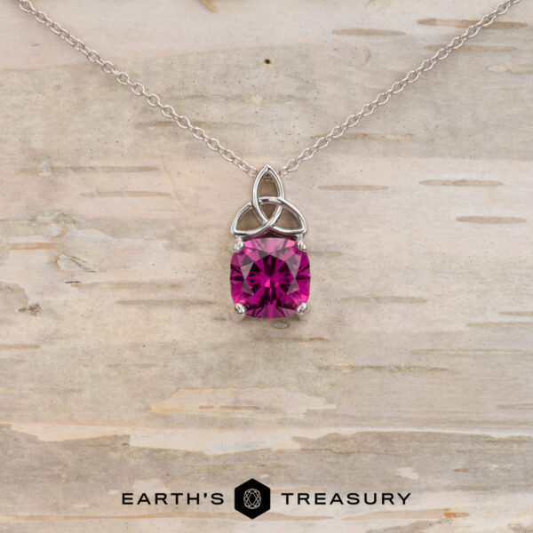 The "Saoirse" pendant in 14K white gold with 1.95-carat Mahenge garnet The "Saoirse" pendant in 14K white gold features a Celtic knot design and a 1.95-carat Mahenge garnet, shown against light wood with the Earth's Treasury logo. Ideal for anyone looking for unique, custom jewelry.
