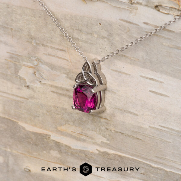 The "Saoirse" pendant in 14K white gold with 1.95-carat Mahenge garnet The "Saoirse" pendant in 14K white gold features a Celtic knot design and a 1.95-carat Mahenge garnet, shown on light wood with the "Earth's Treasury" logo—ideal for custom jewelry enthusiasts.