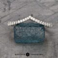 The Chevron Tapered Pave Diamond Band in platinum stands on a rough blue gemstone, set against a geometric background with the "Earth's Treasury" logo below.