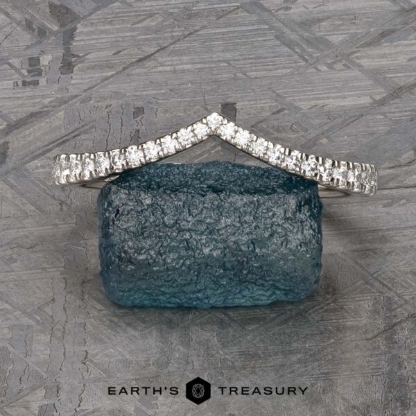 The Chevron Tapered Pave Diamond Band in platinum The Chevron Tapered Pave Diamond Band in platinum stands on a rough blue gemstone, set against a geometric background with the "Earth's Treasury" logo below.