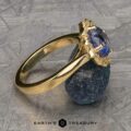 The "Mirabelle" ring in 18K yellow gold with a 1.92-carat Ceylon sapphire is displayed on a rough blue stone, set against a textured gray background with the Earth's Treasury logo at the bottom.