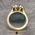 The "Mirabelle" ring in 18K yellow gold with a 1.92-carat Ceylon sapphire is displayed upright on a textured dark stone, with the Earth's Treasury logo at the bottom.