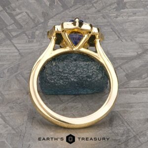 The "Mirabelle" ring in 18K yellow gold with a 1.92-carat Ceylon sapphire is displayed upright on a textured dark stone, with the Earth's Treasury logo at the bottom.