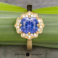 The "Mirabelle" ring in 18K yellow gold, featuring a 1.92-carat Ceylon sapphire surrounded by diamonds, rests on a green leaf. The text "EARTH'S TREASURY" appears below.