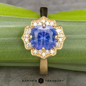 The "Mirabelle" ring in 18K yellow gold, featuring a 1.92-carat Ceylon sapphire surrounded by diamonds, rests on a green leaf. The text "EARTH'S TREASURY" appears below.