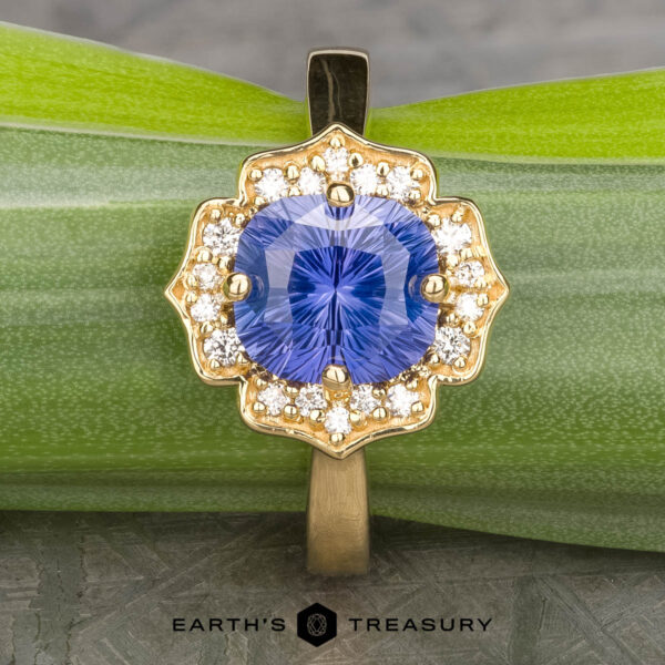The "Mirabelle" ring in 18K yellow gold with 1.92-Carat Ceylon sapphire The "Mirabelle" ring in 18K yellow gold, featuring a 1.92-carat Ceylon sapphire surrounded by diamonds, rests on a green leaf. The text "EARTH'S TREASURY" appears below.