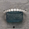The Tapered Prong-Set Diamond Contour Band in 14K white gold rests on a rough blue stone surface, with the Earth's Treasury logo displayed below.