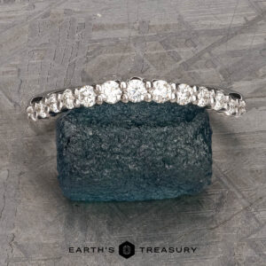 The Tapered Prong-Set Diamond Contour Band in 14K white gold rests on a rough blue stone surface, with the Earth's Treasury logo displayed below.