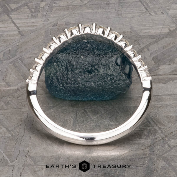 The Tapered Prong-Set Diamond Contour Band in 14K white gold The Tapered Prong-Set Diamond Contour Band in 14K white gold, featuring rectangular diamonds along the band, is displayed upright on a textured gray surface with the Earth's Treasury logo at the bottom.