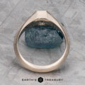 The "Gawain" ring, crafted in unplated 18k palladium white gold with a 0.79-carat Montana sapphire, is shown upright on a textured gray surface. The Earth's Treasury logo appears at the bottom.