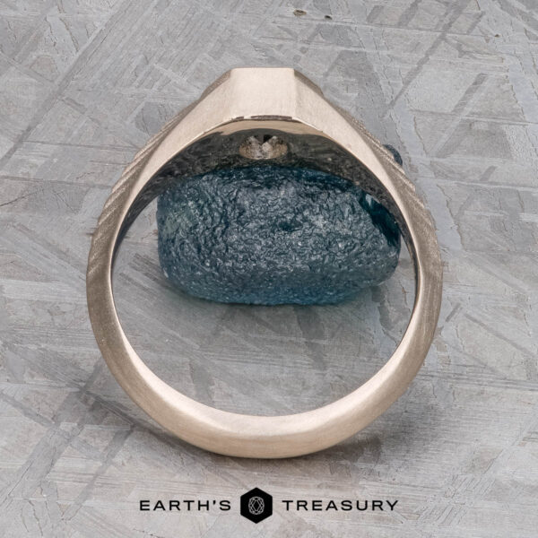 The "Gawain" ring in unplated 18k palladium white gold with 0.79-Carat Montana sapphire The "Gawain" ring, crafted in unplated 18k palladium white gold with a 0.79-carat Montana sapphire, is shown upright on a textured gray surface. The Earth's Treasury logo appears at the bottom.