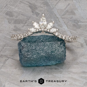 The Pave "Vilaine" band in 14K white gold, set with marquise-cut diamonds, rests on rough blue-green mineral atop a textured gray surface, displayed above the “EARTH’S TREASURY” logo.