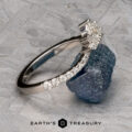 The Pave "Vilaine" band in 14K white gold, set with marquise-cut diamonds, rests on rough blue-green mineral atop a textured gray surface, displayed above the “EARTH’S TREASURY” logo.